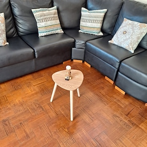 Ein modernes Wohnzimmer mit einem schwarzen Ledersofa, einem runden Couchtisch aus Holz und gemusterten Zierkissen.