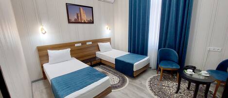 Una habitación de hotel con dos camas, una mesita pequeña con una silla y una alfombra decorativa.