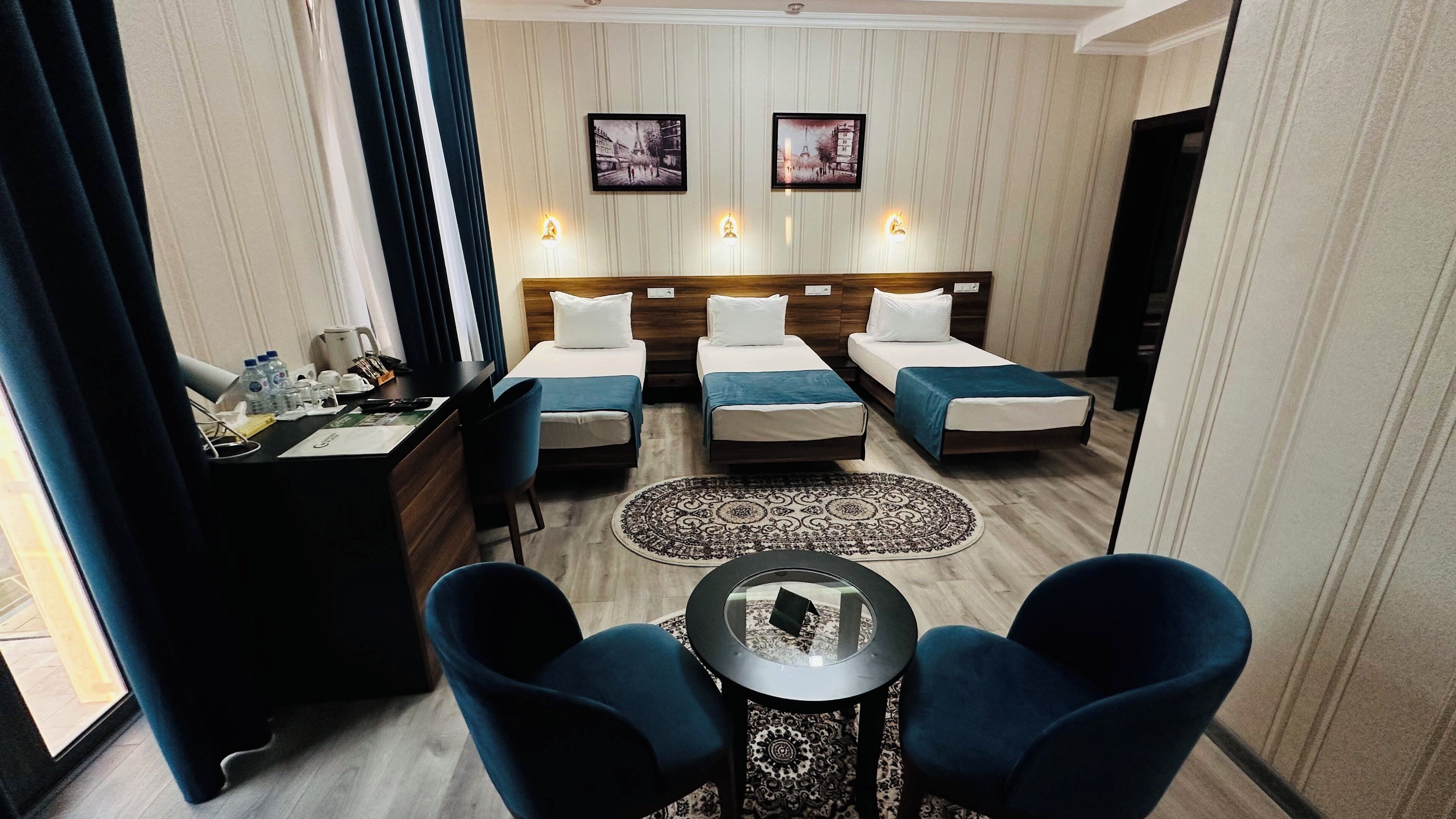 Habitación de hotel con dos camas, un escritorio con una silla, una mesa redonda y dos sillones.