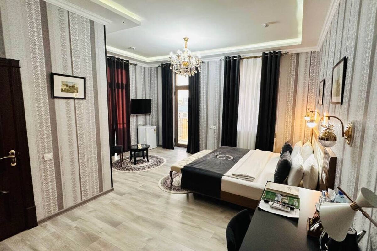 Ein Hotelzimmer mit Bett, Schreibtisch, Stuhl, einer Kandelaber und Vorhängen.