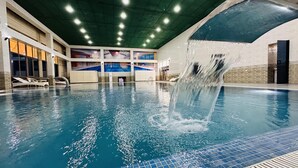 An indoor swimming pool with clear water, a waterfall feature, and a modern architectural design with a high ceiling and bright lighting. - Garden Plaza Bukhara (Bukhara)
