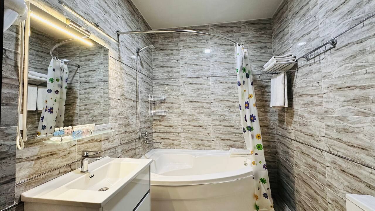 Ein modernes Badezimmer mit Marmorwand, einer Badewanne, einem Waschbecken und einem Duschvorhang mit Blumenmuster.