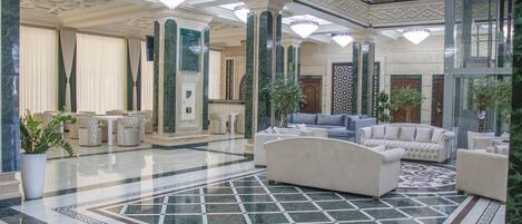 A spacious lobby with a marble floor, elegant furniture, and decorative chandeliers.