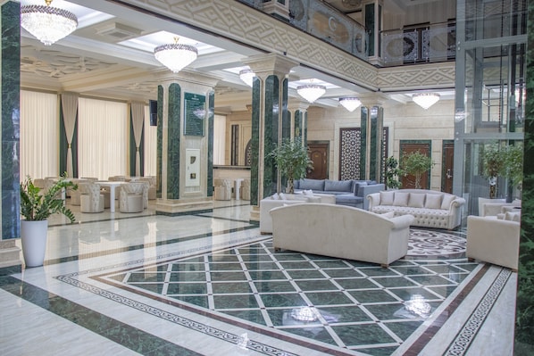 A spacious lobby with a marble floor, elegant furniture, and decorative chandeliers.