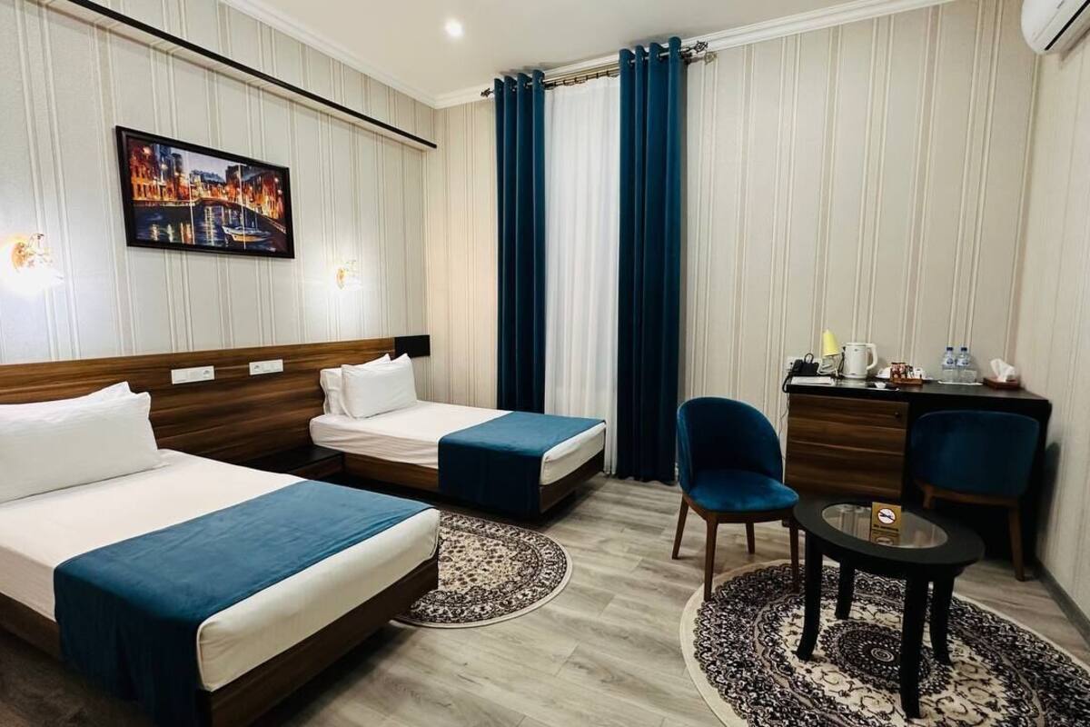 Ein Hotelzimmer mit zwei Betten, einem Schreibtisch, einem Sessel, einem Fernseher und einem Bild an der Wand.