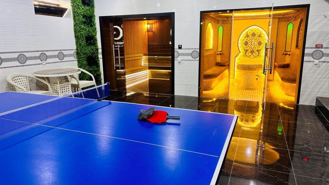 A ping pong table with a blue surface and a red paddle, surrounded by a white wall with a decorative pattern.