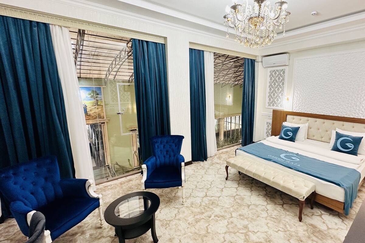 Ein Schlafzimmer mit einem großen Bett, zwei blauen Sessel, einem kleinen runden Tisch und einer Pendelleuchte.