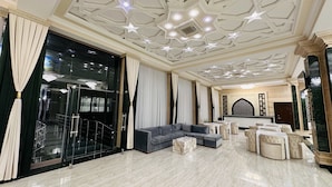 A spacious living area with a grey sectional sofa, marble coffee table, and a large window with curtains. - Garden Plaza Bukhara (Bukhara)
