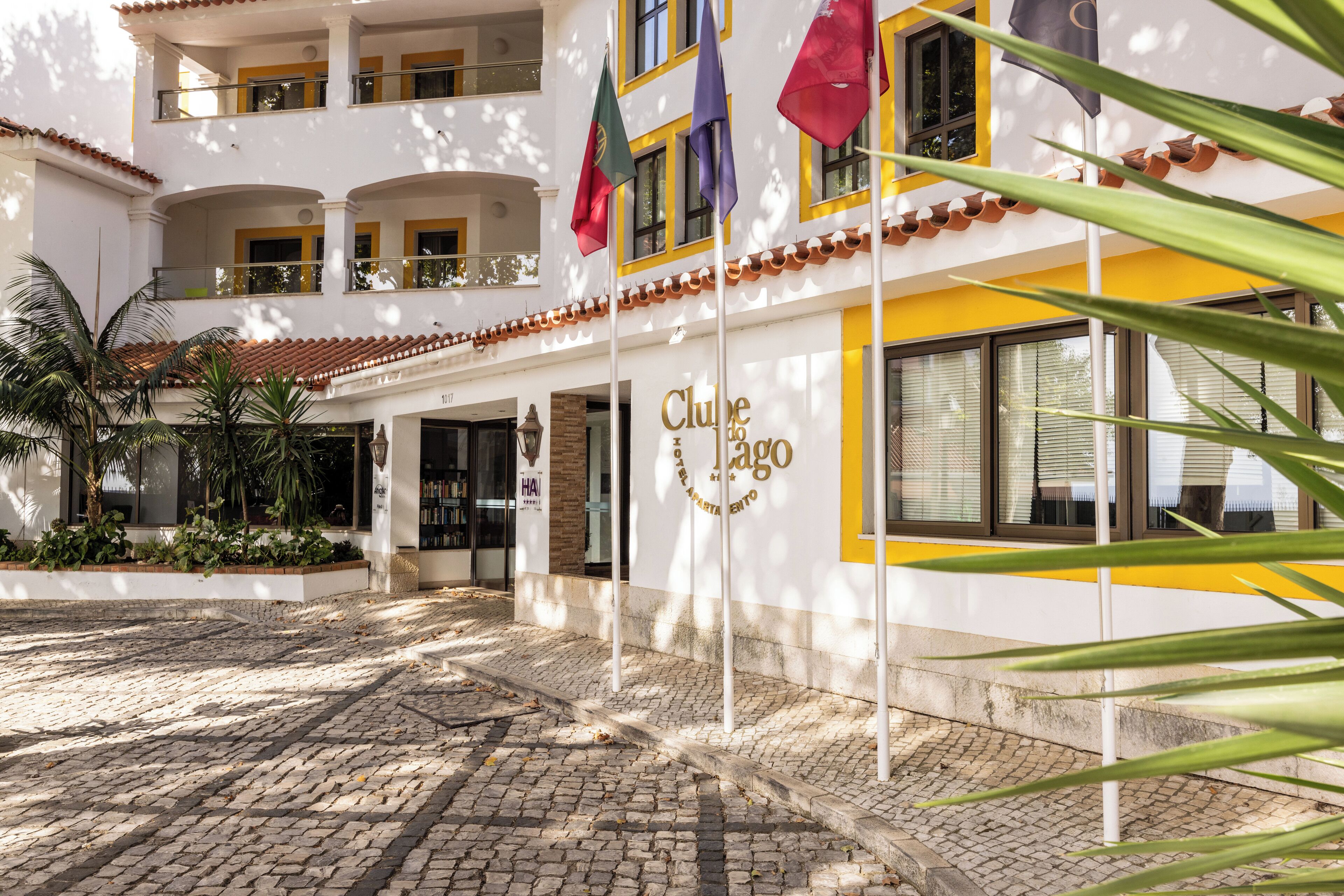 Entrada de un hotel con un camino adoquinado, varios balcones y banderas.