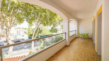 A balcony with a tiled floor, a view of a street with cars, and a green table with chairs.