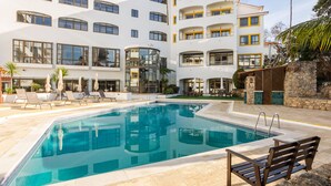 A modern hotel with a swimming pool, lounge chairs, and a stone wall. - Clube do Lago Hotel (Cascais)