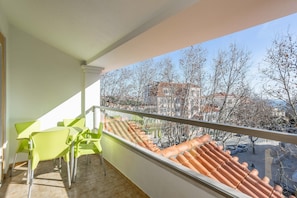 Un balcón con vistas a la ciudad, suelo de baldosas y dos sillas verdes.