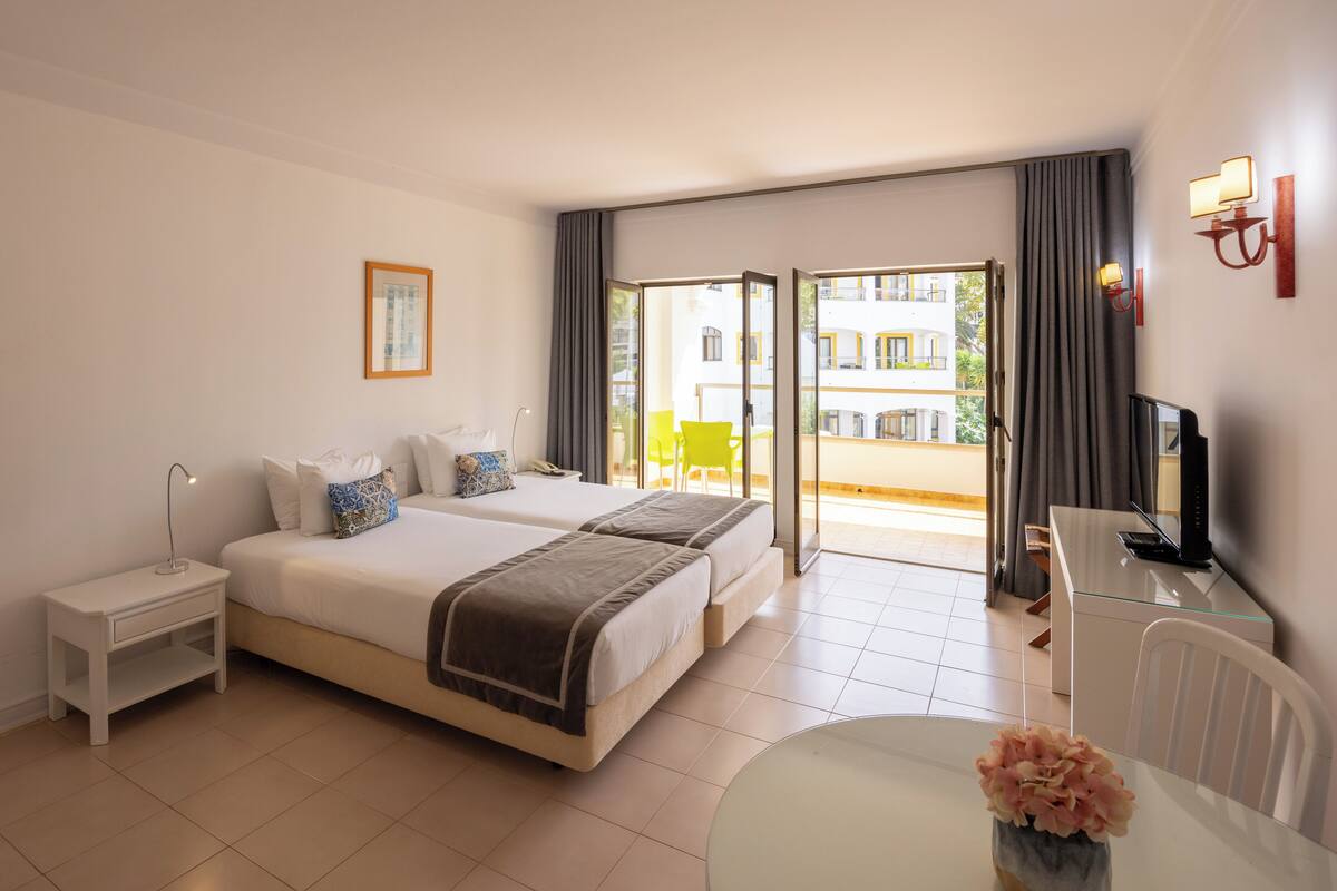A hotel room with two beds, a desk, a chair, a small table, and a TV.