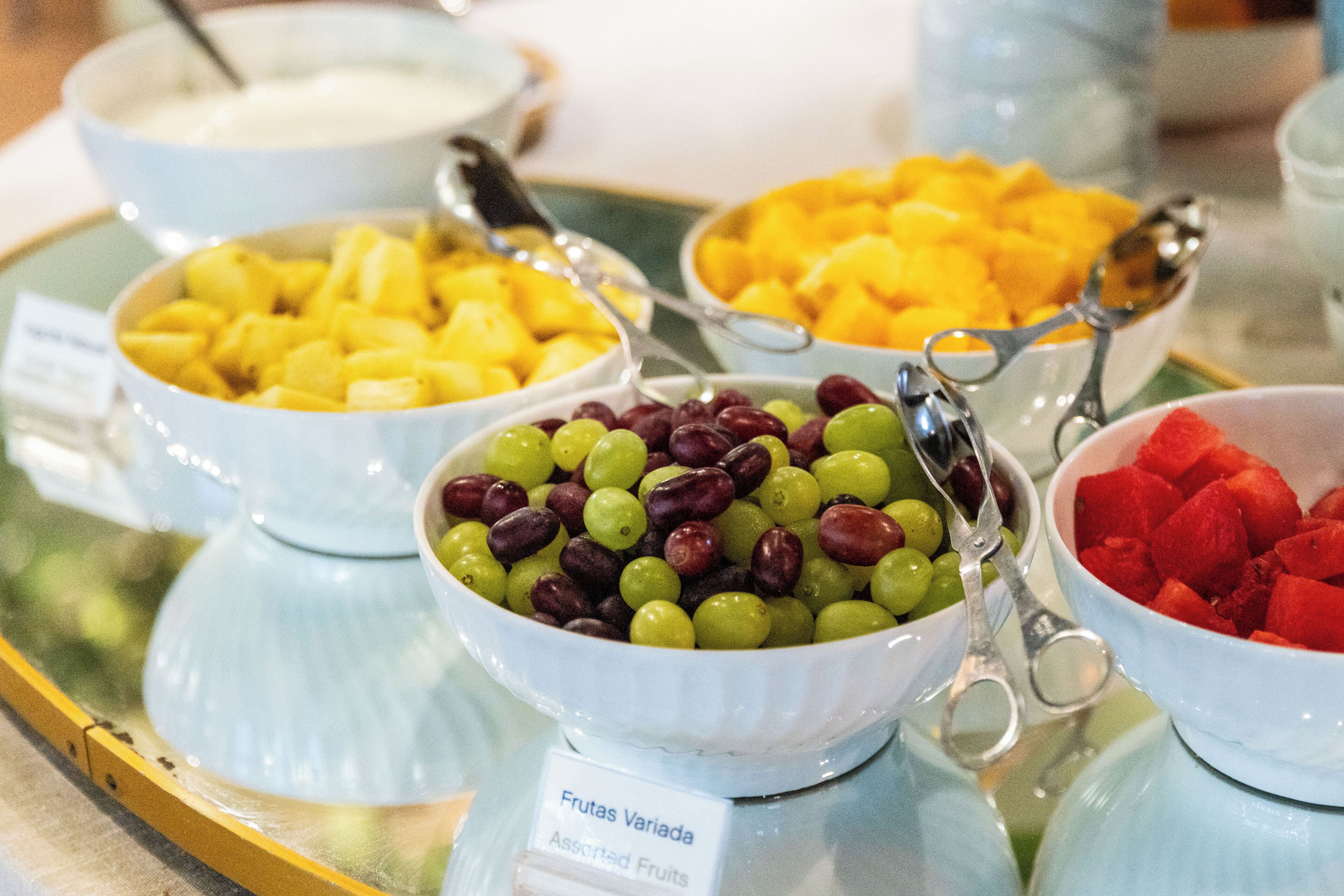 Un bufé con diferentes fuentes de fruta, incluyendo uvas, mangos y sandía.