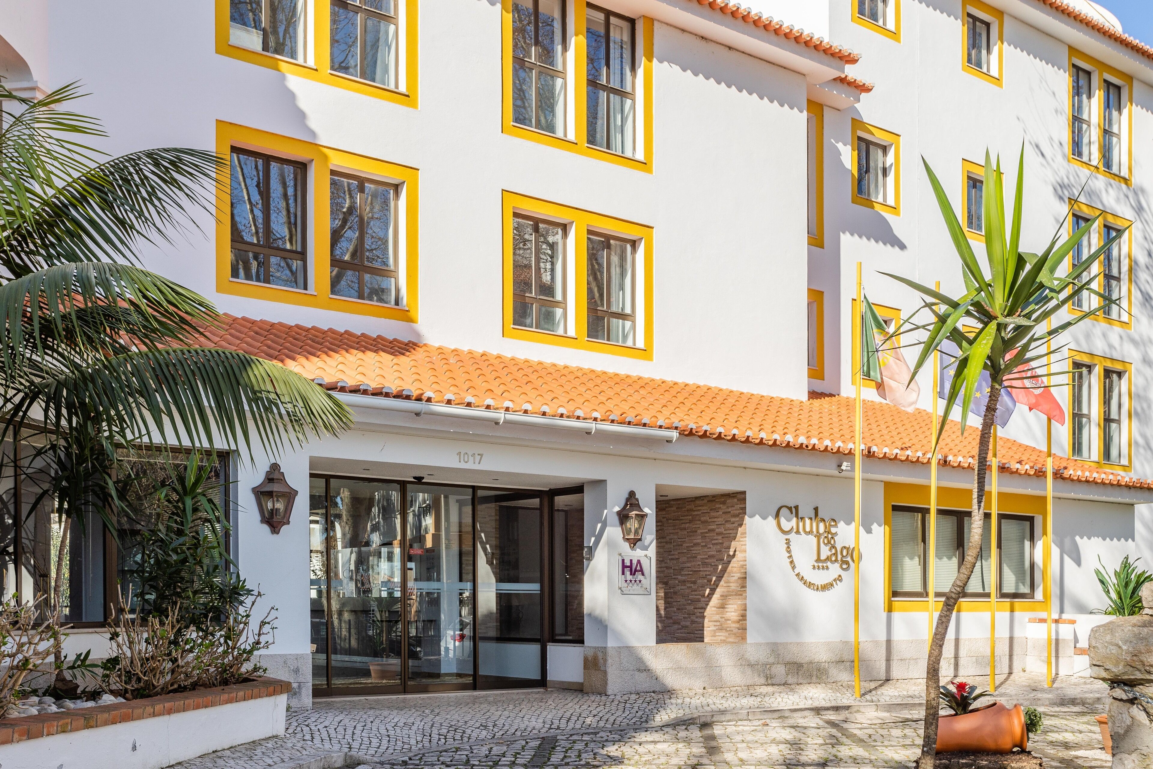 A white building with yellow trim and a tiled roof, featuring a sign that reads "Clube Lago."
