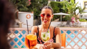 A person sitting at an outdoor table with a drink, surrounded by a pool and greenery. - Clube do Lago Hotel (Cascais)