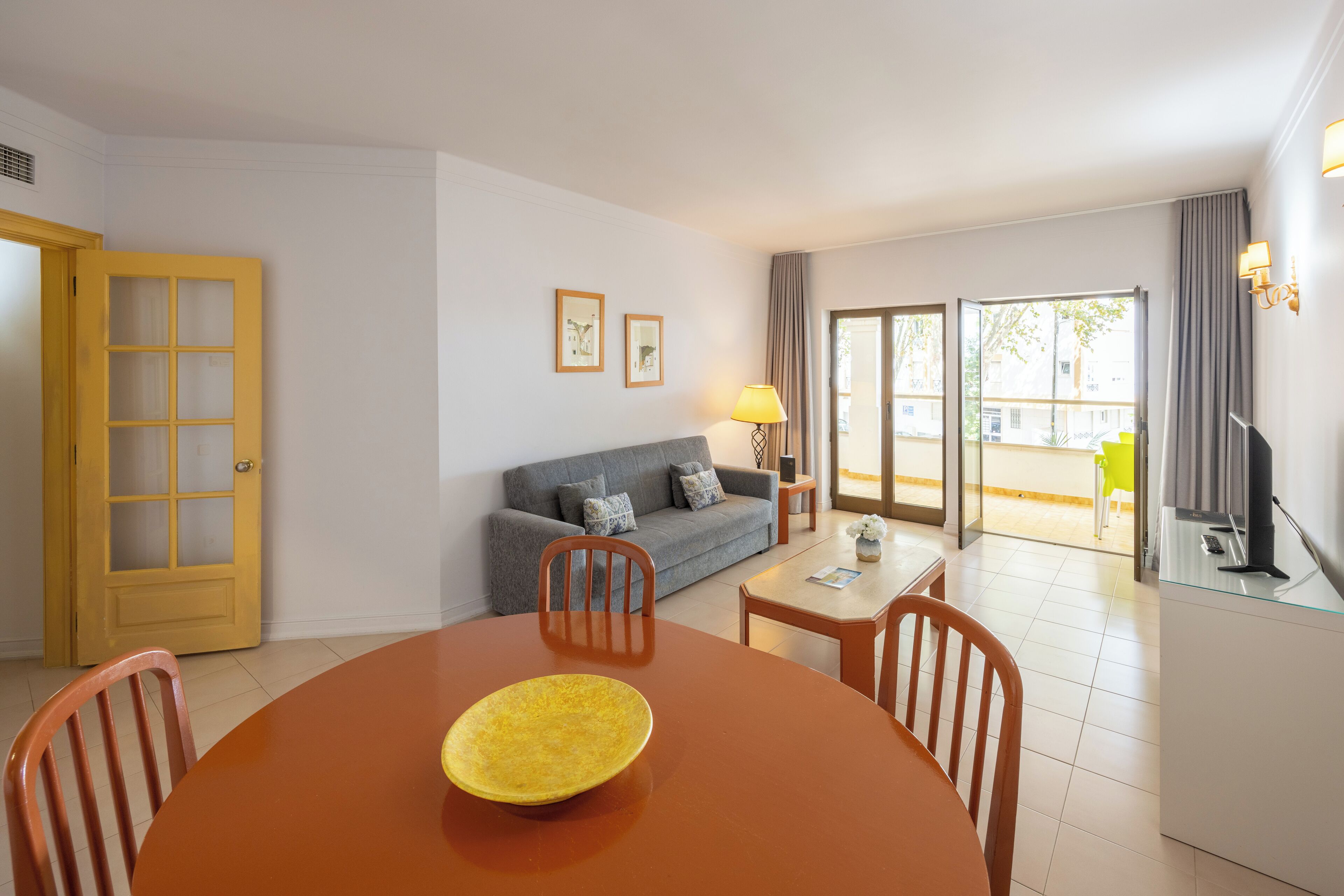 Un salon avec un canapé, une table à manger avec des chaises, un bol jaune et un téléviseur.