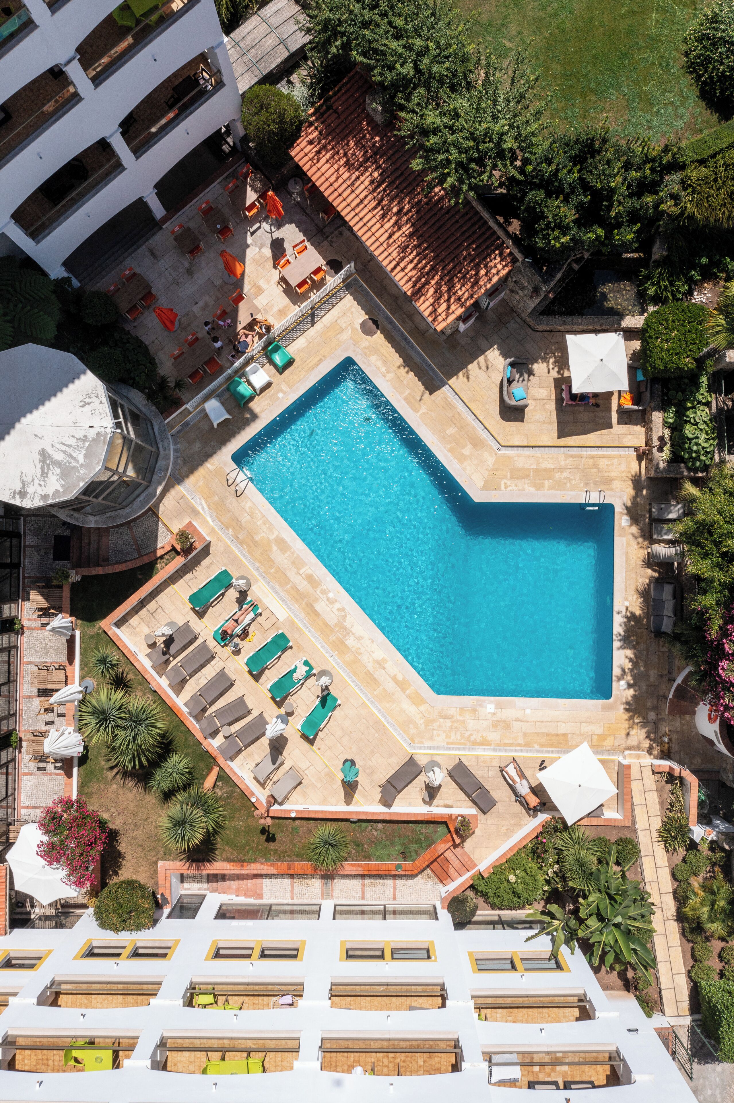An aerial view of a hotel with a swimming pool, sun loungers, and a rooftop terrace.