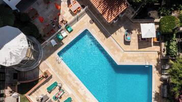 An aerial view of a hotel with a swimming pool, sun loungers, and a rooftop terrace.