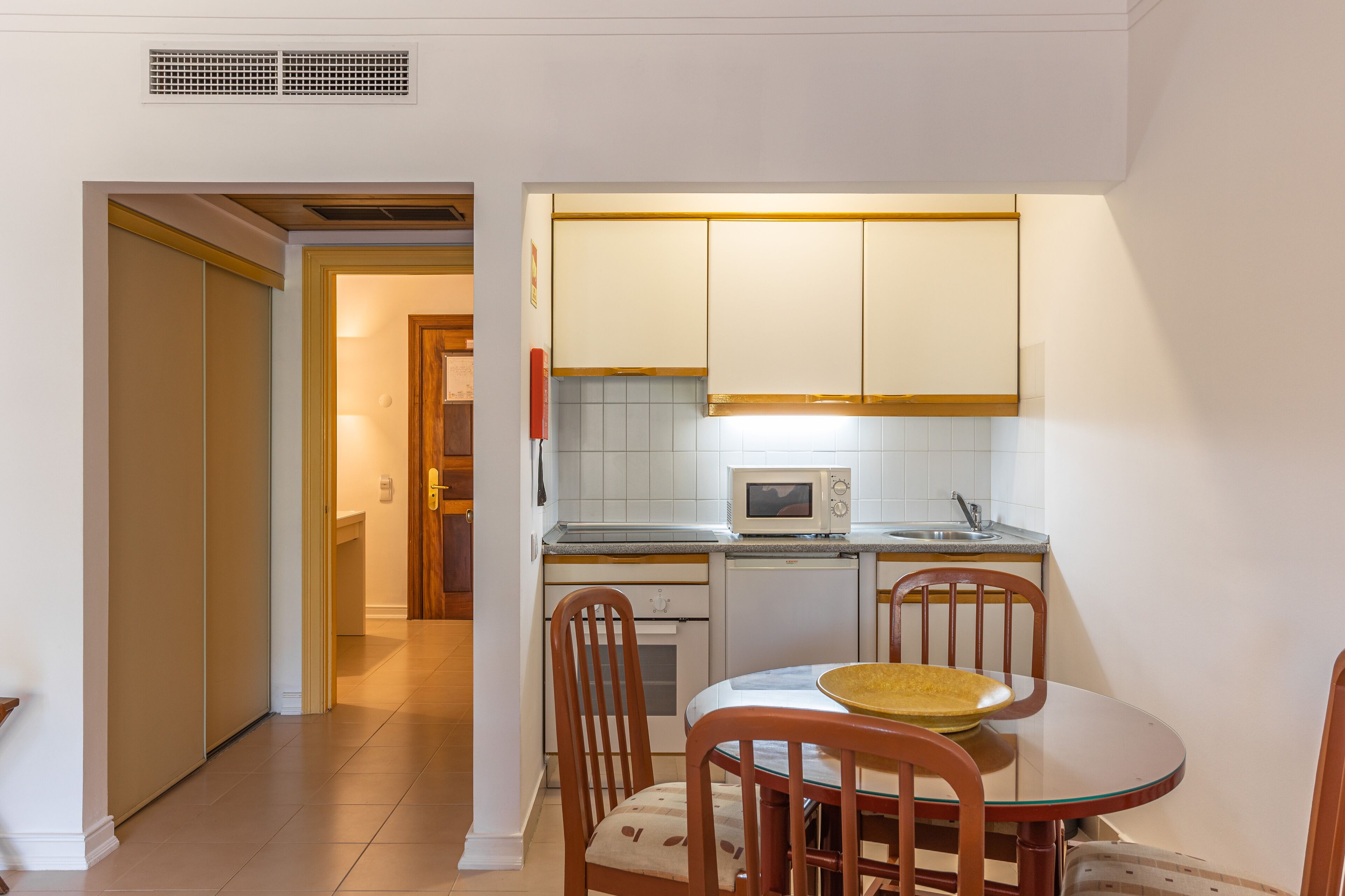 Une cuisine compacte avec des meubles blancs, un four à micro-ondes, un évier et un coin repas comprenant une table et des chaises.
