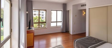 Una habitación de hotel moderna con un ventanal grande, una cama, un televisor y un escritorio pequeño.