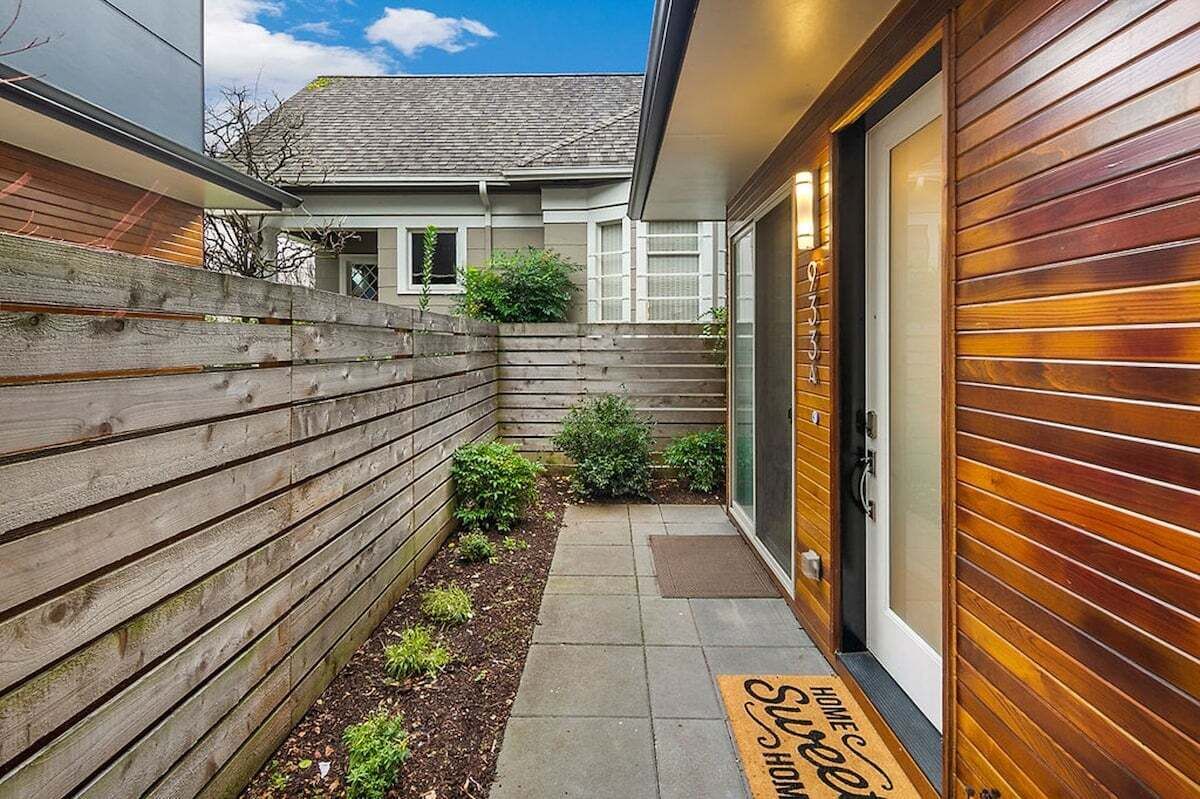 A modern house with a wooden fence, a small garden, and a door with a doormat.