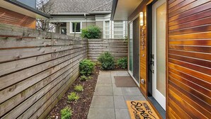 Una casa moderna con cerca de madera, un pequeño jardín y una puerta con felpudo.