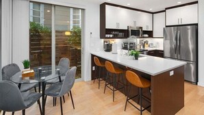 Una cocina moderna con una isla central, taburetes de bar y una mesa de comedor con sillas.