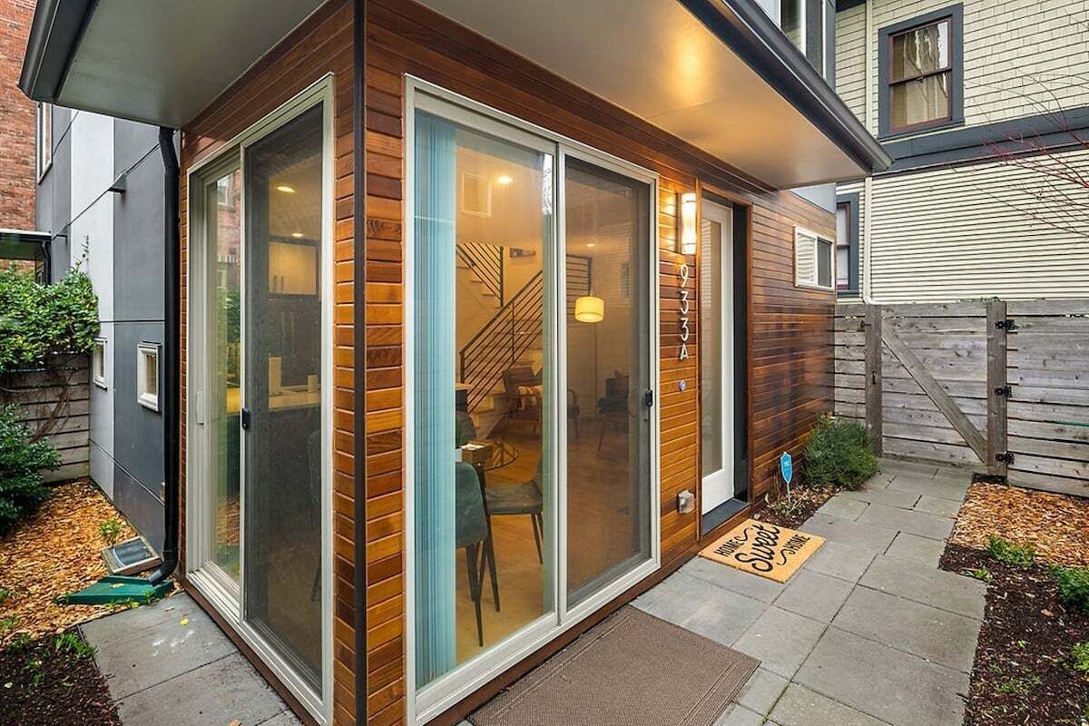 A modern house with a glass door entrance, a visible staircase, and a small garden area with a doormat.