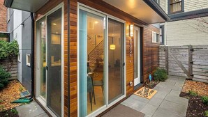 Una casa moderna con puerta de cristal, escalera visible y un pequeño jardín con felpudo.
