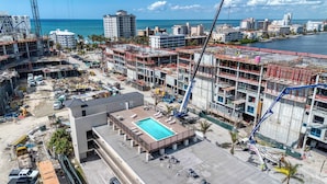 A hotel with a rooftop pool, construction cranes, and a view of the ocean. - Modern Condo With Pool Steps From Vanderbilt Beach (Naples)