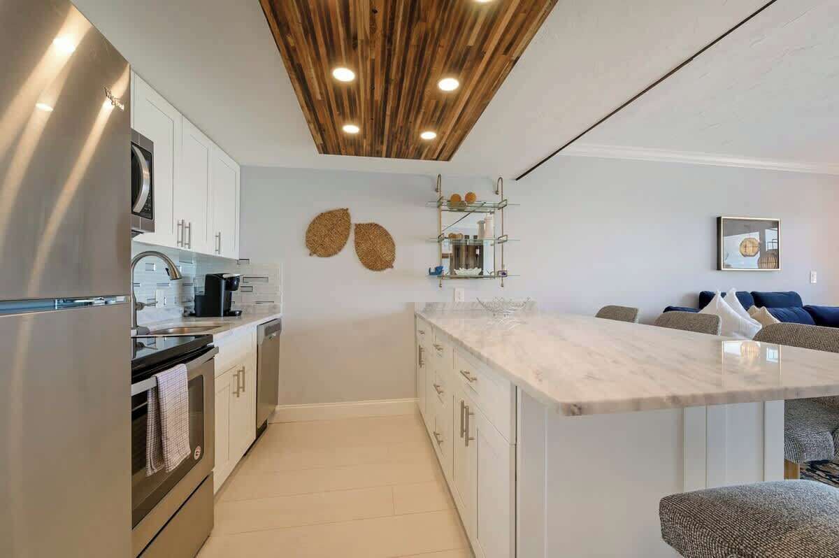 A modern kitchen with stainless steel appliances, a wooden ceiling, and a central island.