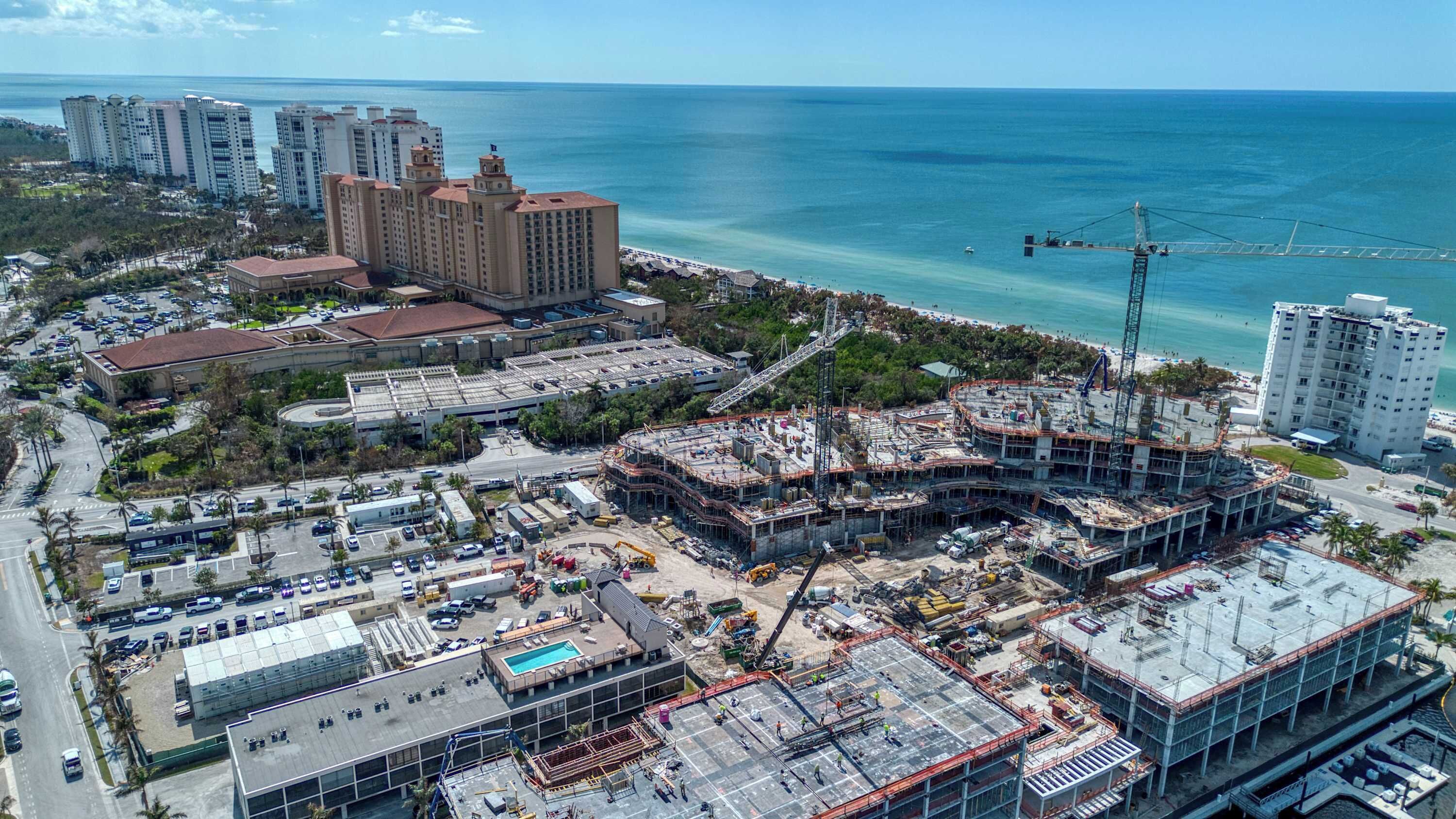 A large hotel with multiple floors, a swimming pool, and a view of the ocean.