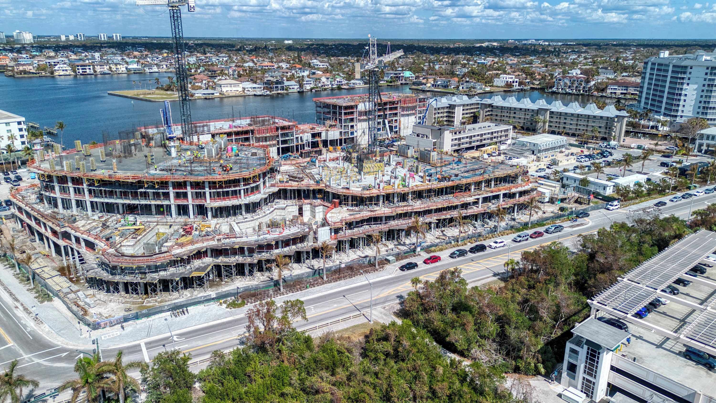 A multi-story hotel with a waterfront view, under construction with visible scaffolding and cranes.