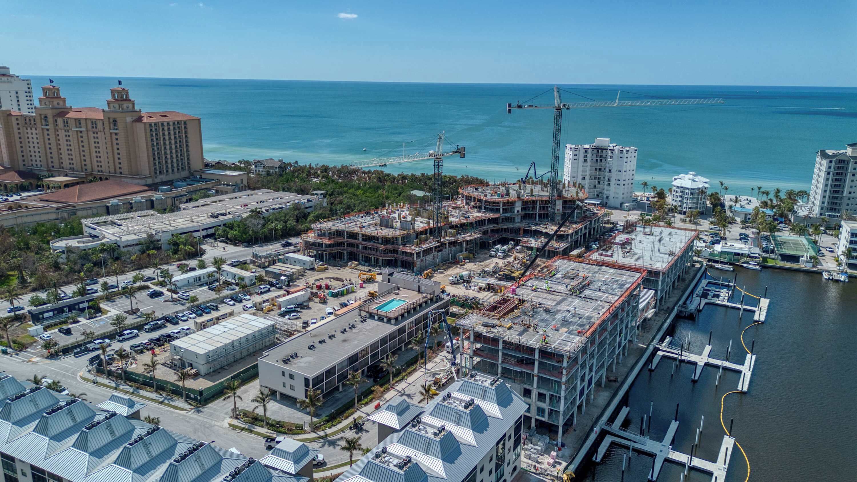 Vista aérea de una zona costera con un gran hotel en construcción, un puerto deportivo y un puente al fondo.