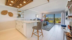 A modern kitchen with a bar area, a dining space with a view, and a balcony with a railing. - Modern Condo With Pool Steps From Vanderbilt Beach (Naples)