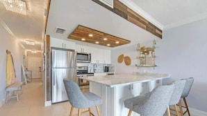 A modern kitchen with a central island, stainless steel appliances, and a wooden ceiling accent. - Modern Condo With Pool Steps From Vanderbilt Beach (Naples)