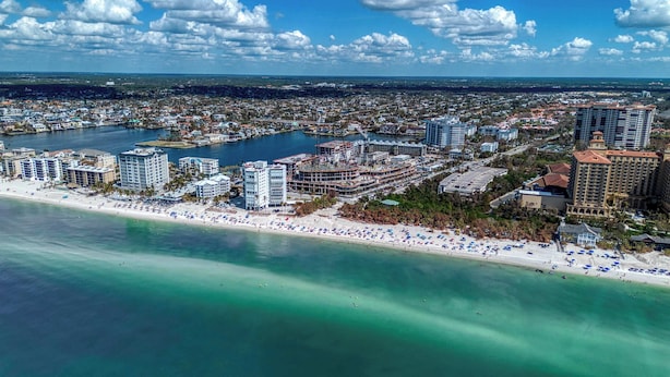 An aerial view of a coastal city with a beachfront, high-rise hotels, and a marina. - Modern Condo With Pool Steps From Vanderbilt Beach (Naples)