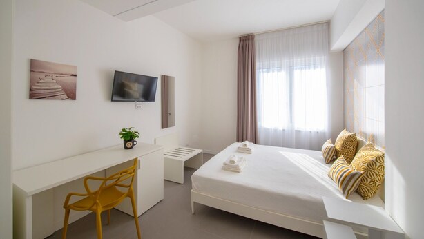 A modern hotel room with a bed, a desk, a chair, a TV, and a window with curtains. - Gemmis in Pompeii (Pompei)