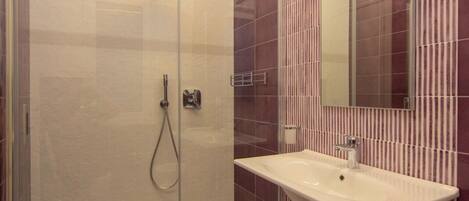 A modern bathroom with a glass-enclosed shower, a white sink, and a striped tile backsplash.