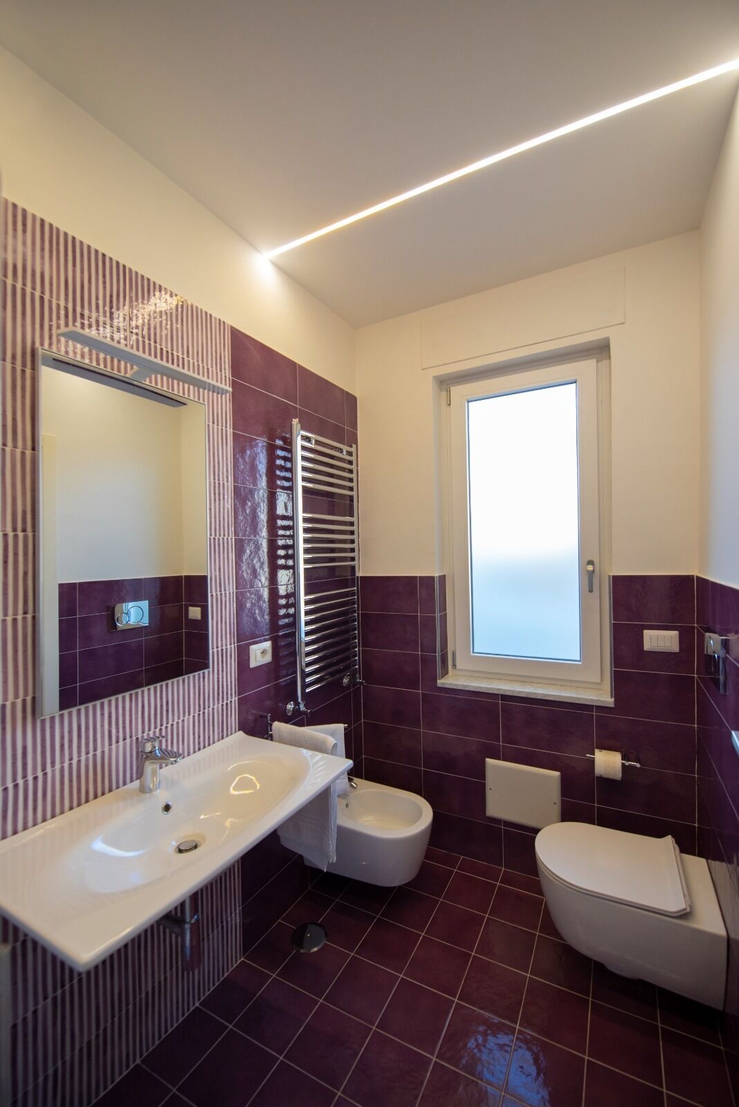 A modern bathroom with a large mirror, a white sink, a bidet, and a toilet.