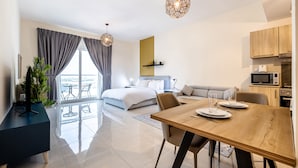 Una habitación de hotel moderna con una cama grande, una zona de comedor, una cocina y un balcón con vistas.
