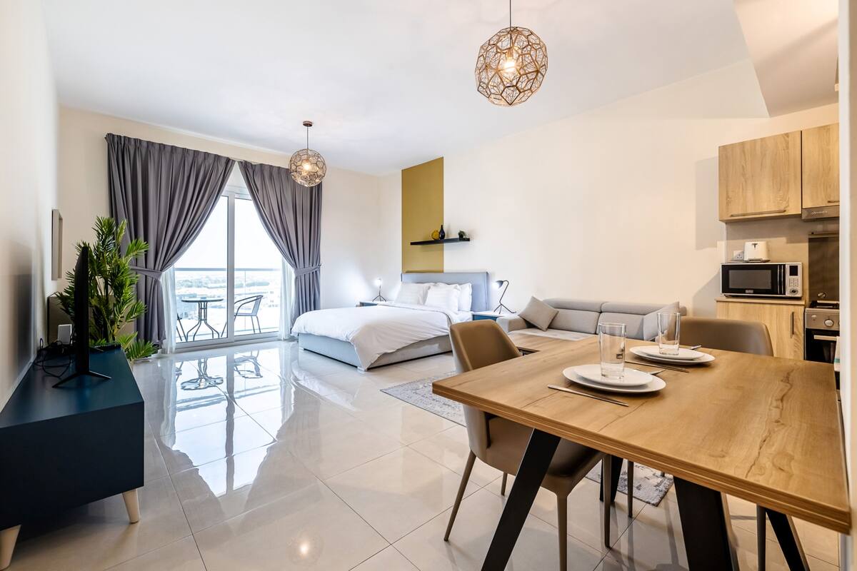 Een moderne hotelkamer met een groot bed, een eethoek, een keuken en een balkon met uitzicht.