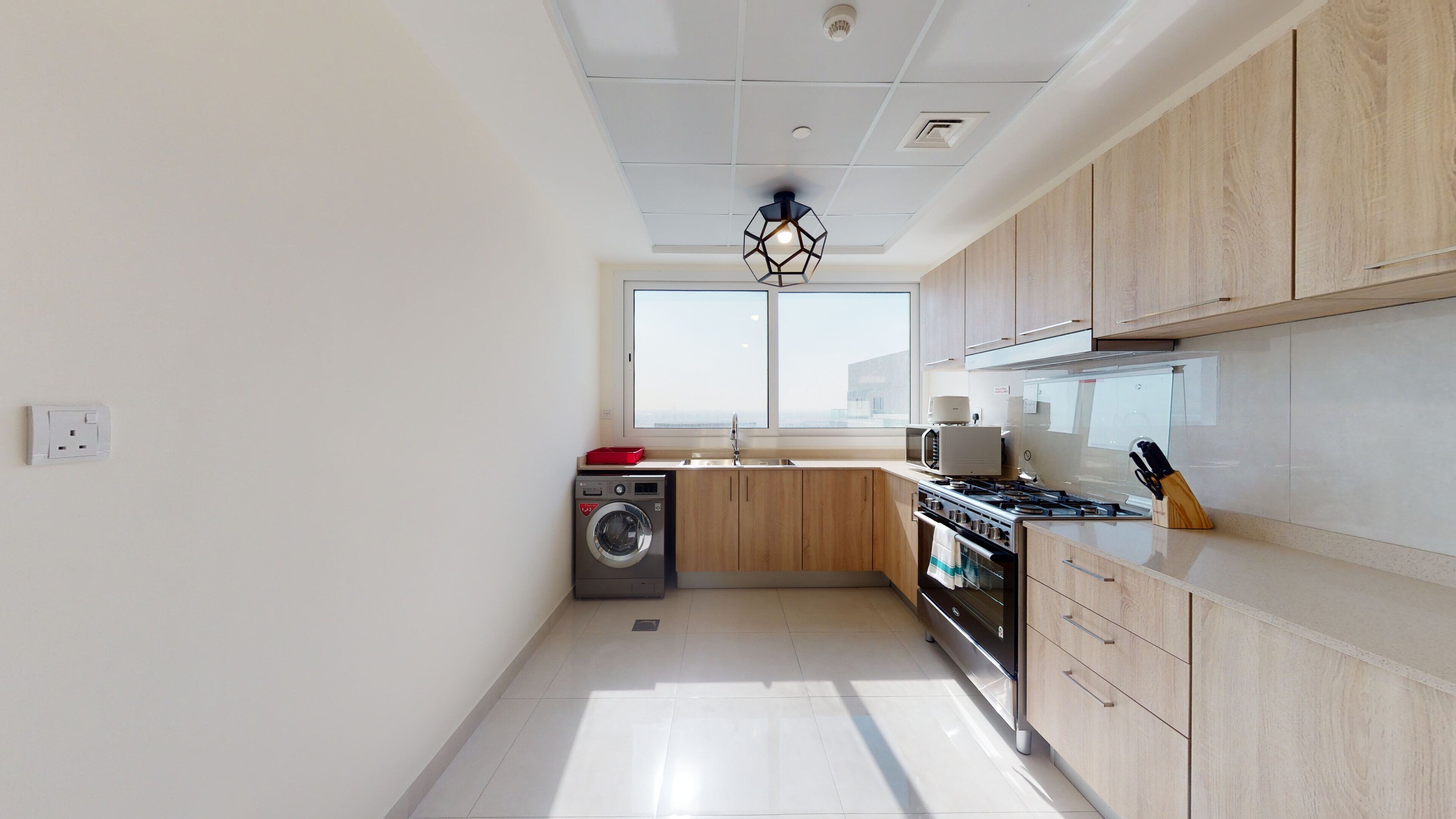 A modern kitchen with wooden cabinets, a built-in washing machine, a gas stove, and a window providing natural light.