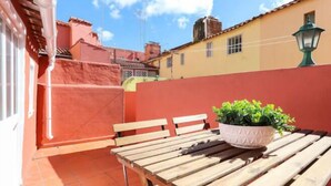A patio with a wooden table and benches, a potted plant, and a red wall. - Santa Marta Apartment by Trip2Portugal (Lisbon)