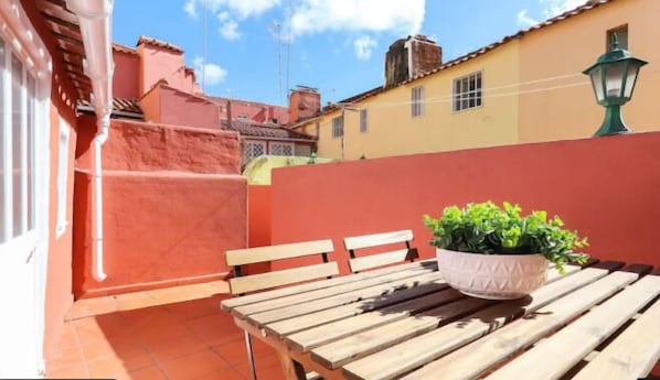 Une terrasse avec une table et des bancs en bois, une plante en pot et un mur rouge.
