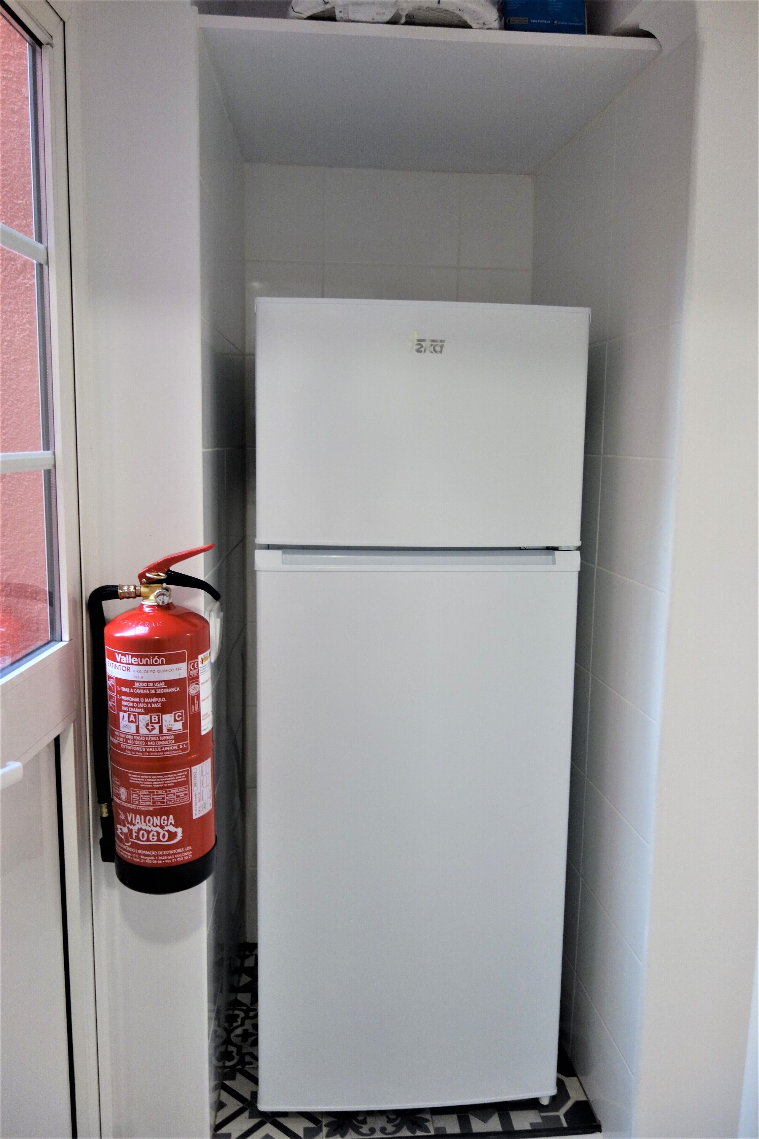 Un refrigerador blanco en un pasillo estrecho con un extintor de incendios en la pared.