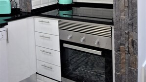 A kitchen with white cabinets, a black countertop, a built-in oven, and a stone backsplash. - Santa Marta Apartment by Trip2Portugal (Lisbon)
