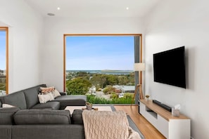 A modern living room with a large window, a grey sofa, a flat-screen TV, and a wooden console table.