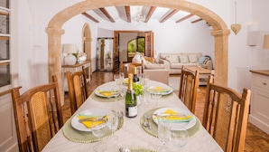 A dining area with a table set for six, a bottle of champagne, and a view of a garden through an open archway. - 3 Bedroom Family Villa in Javea (Javea / Xàbia)